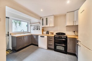 A modern kitchen with a dishwasher, stove, oven, and a window with a view of greenery. - Quaint Cottage in Charming Evesham (Evesham)