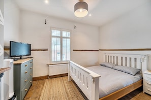 A bedroom with a bed, a dresser, a television, a window with blinds, and a radiator. - Quaint Cottage in Charming Evesham (Evesham)