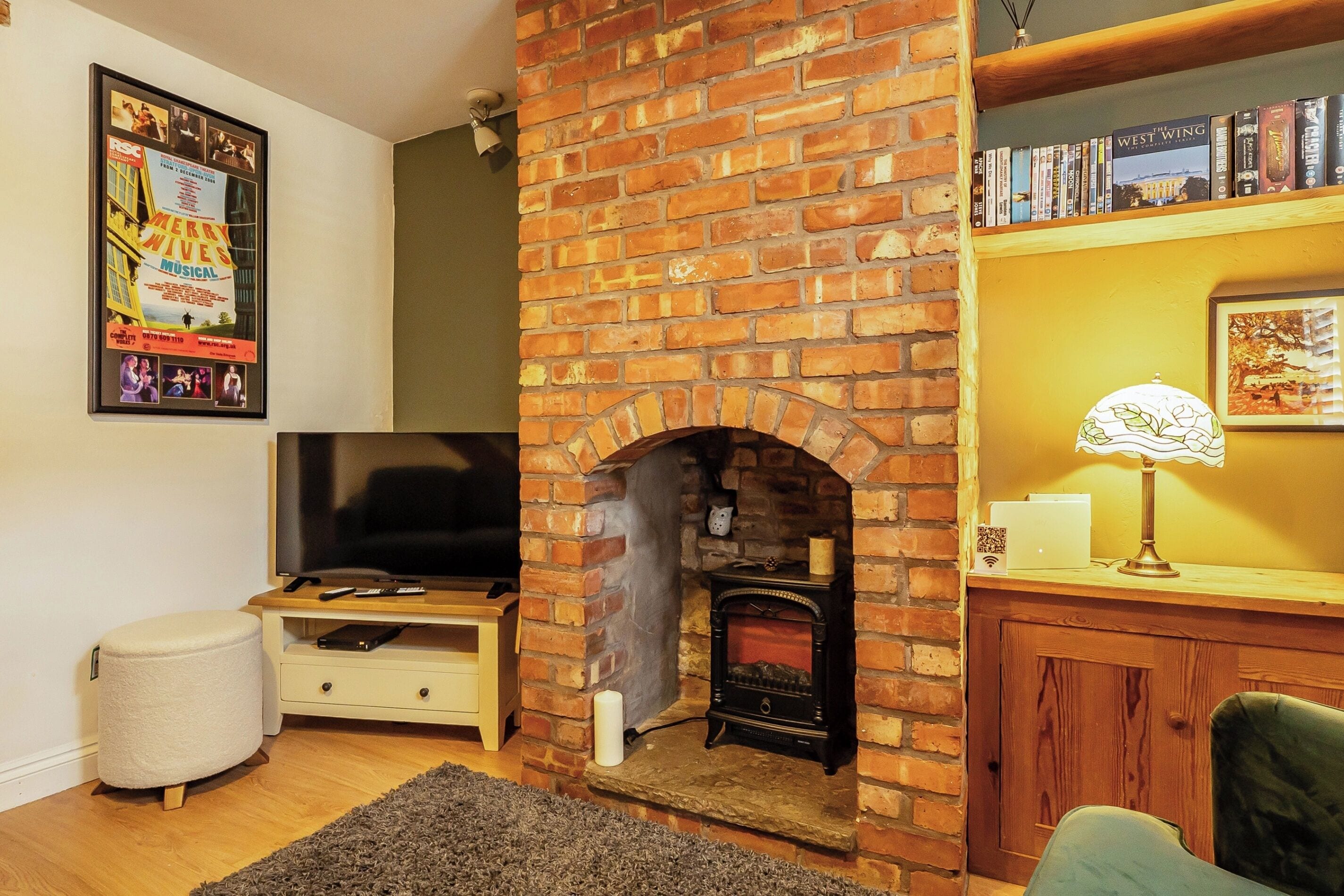 A living room with a brick fireplace, a television, a bookshelf, and a framed picture on the wall.