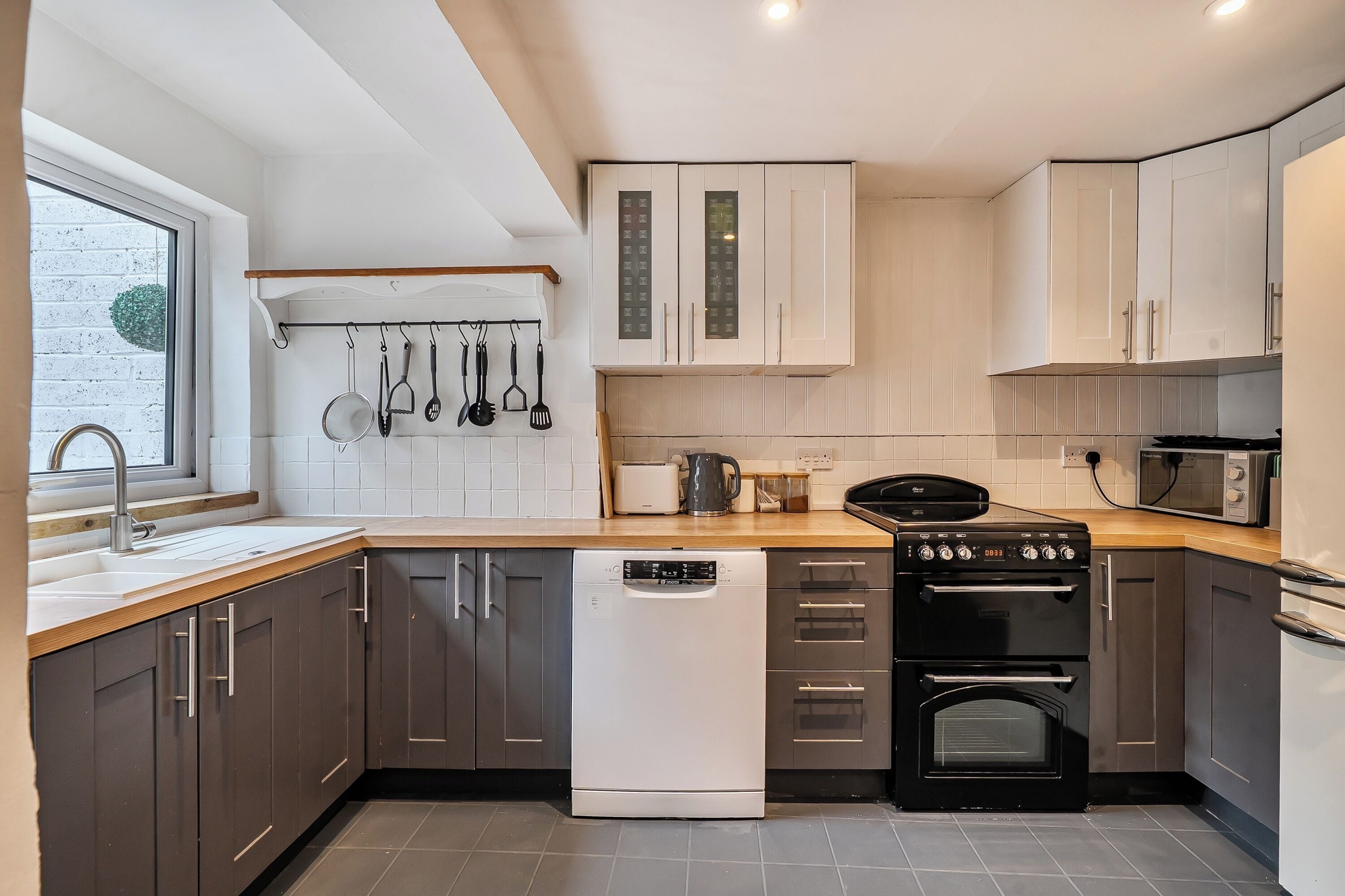 Een moderne keuken met een vaatwasser, oven, magnetron en hangende keukengerei.