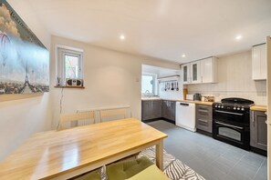 A modern kitchen with a dining area, featuring a wooden table, a radiator, and a stove. - Quaint Cottage in Charming Evesham (Evesham)