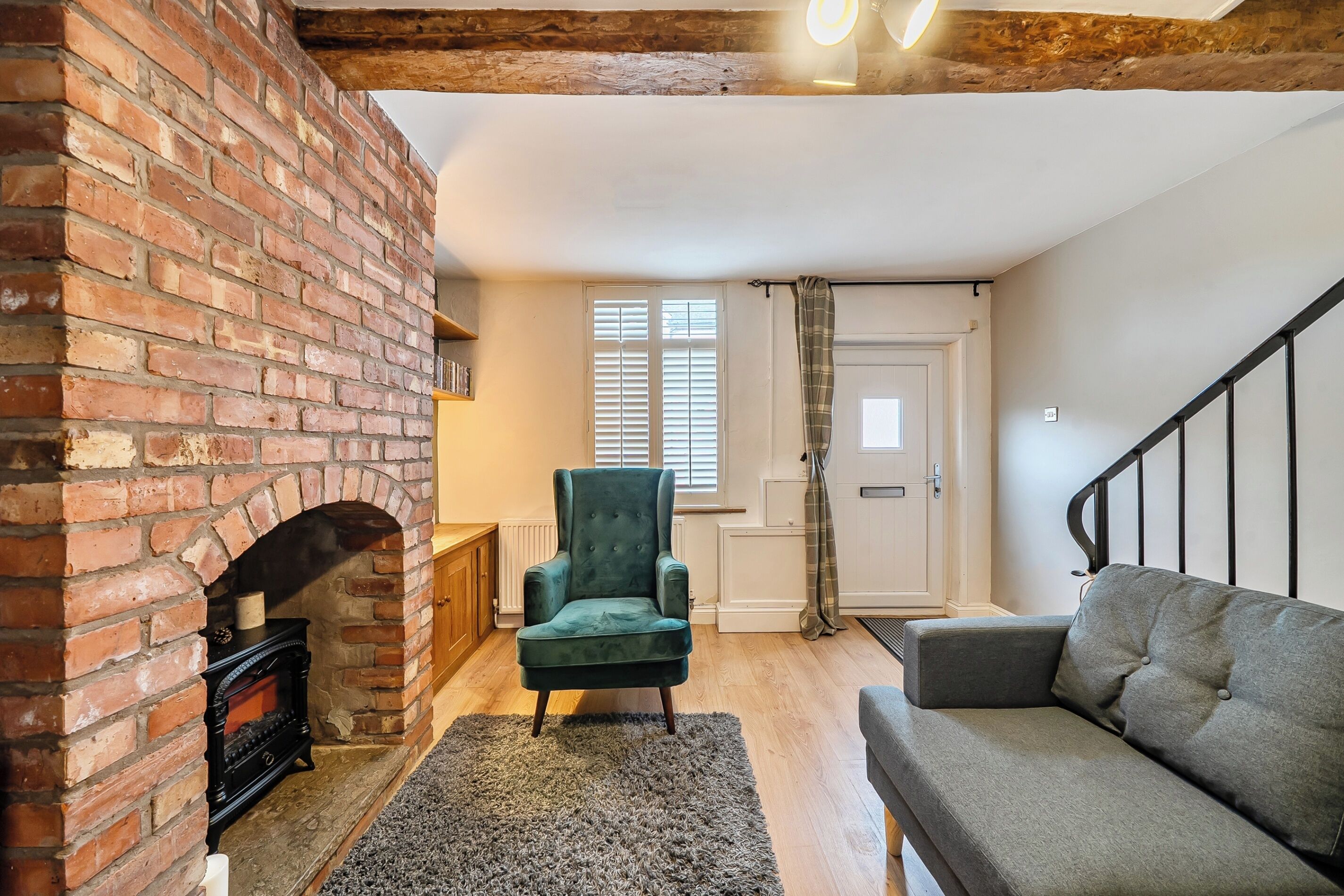 A cozy living room with a brick fireplace, a green armchair, a grey sofa, and a wooden floor.