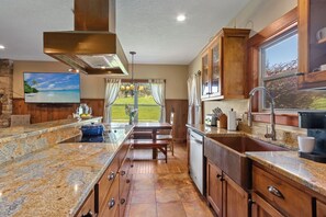 A kitchen with granite countertops, wooden cabinets, a built-in stove, and a large window overlooking a lawn. - Millhouse Lodge | Large Group Retreat | Sleeps 30 (Murphy)