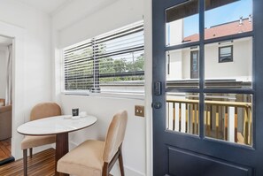 A room with a round table, two chairs, a door with a window, and a view of a building outside. - The Magnolia Suite at One 01 (Savannah)
