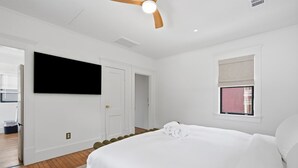 A hotel room with a large bed, a flat-screen TV mounted on the wall, and a window with a blind. - The Magnolia Suite at One 01 (Savannah)