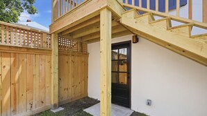 A wooden deck with a staircase leading to a covered area, a wooden fence, and a door with a window. - The Magnolia Suite at One 01 (Savannah)