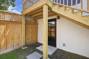 A wooden deck with a staircase leading to a covered area, a wooden fence, and a door with a window. - The Magnolia Suite at One 01 (Savannah)