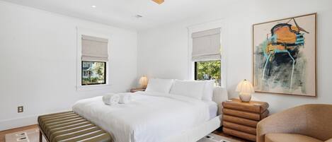 A bedroom with a bed, bedside tables, a bench, a chair, a ceiling fan, and a painting.