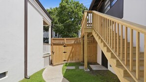 A residential backyard with a wooden staircase leading to a deck, a fenced area, and a concrete pathway. - The Magnolia Suite at One 01 (Savannah)