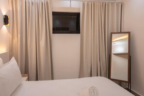 Habitació d'hotel amb un llit, una televisió penjada a la paret i un mirall.