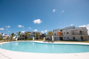 Um hotel moderno com piscina, várias varandas e um céu azul límpido.