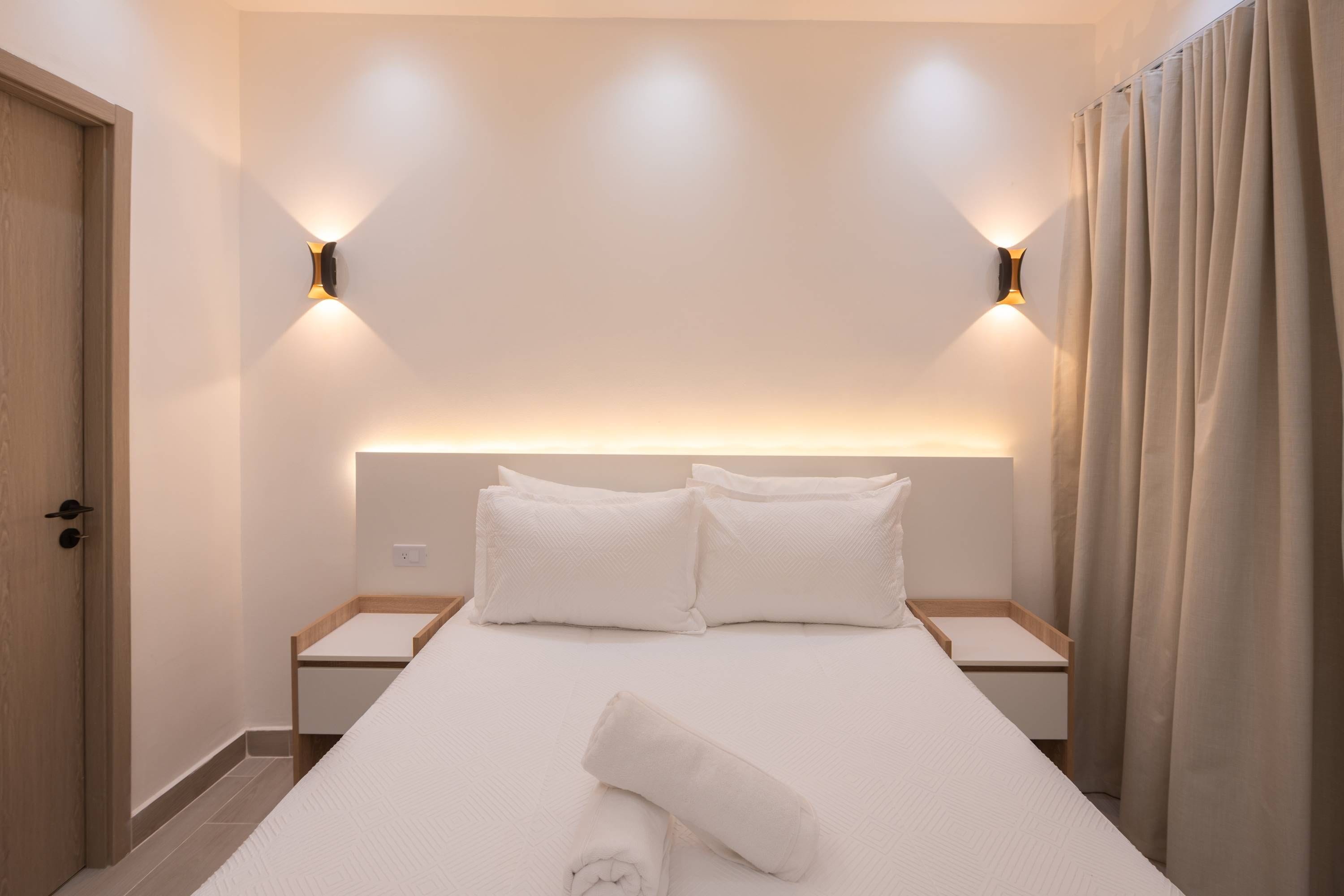 A hotel room with a bed, two bedside tables, a wall-mounted light fixture, and a door.