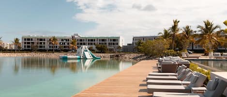 Un espace piscine d’un complexe hôtelier, avec des chaises longues, une terrasse en bois et un bâtiment en arrière-plan.