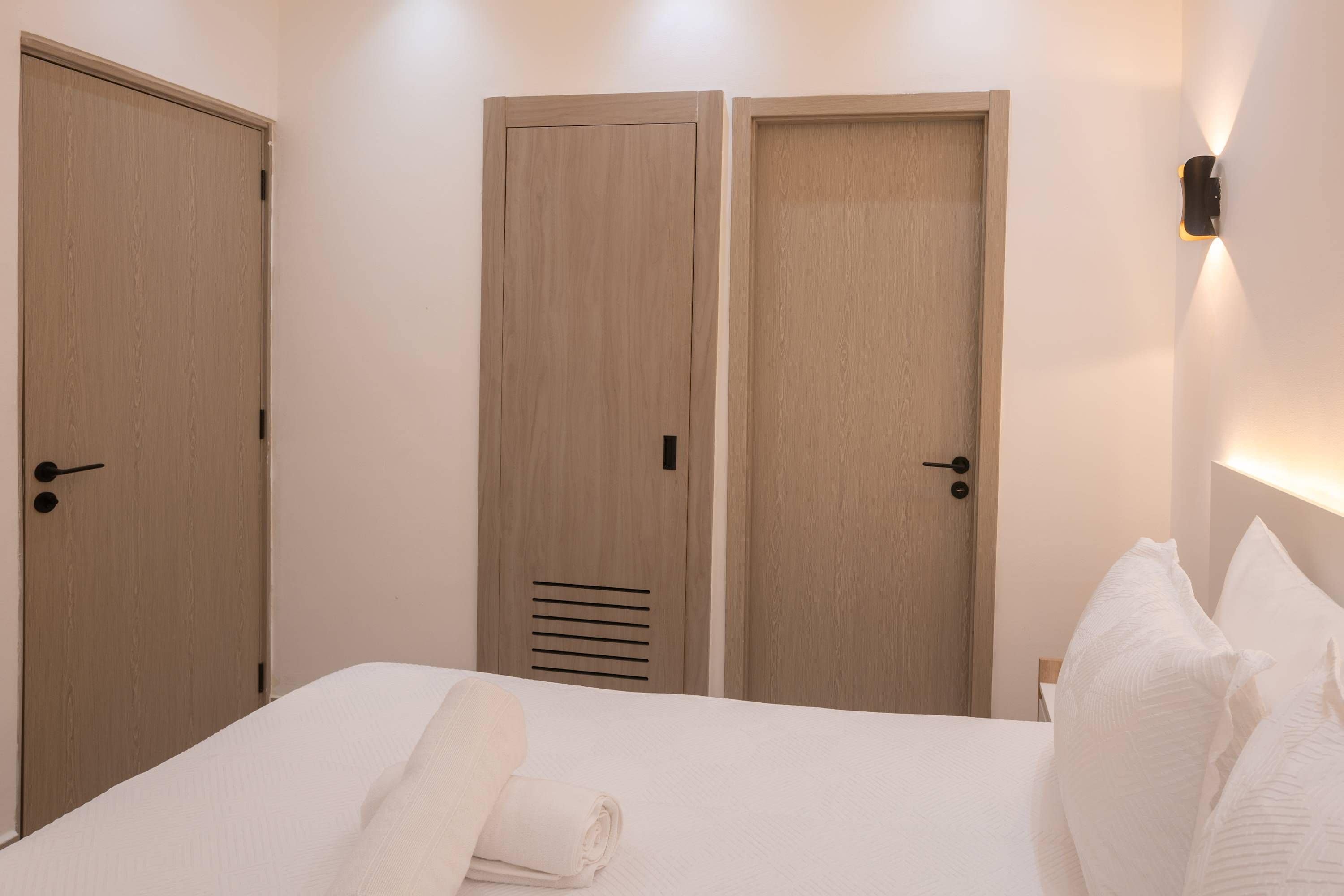 Una habitación de hotel con una cama, dos puertas de madera y una lámpara fijada a la pared.
