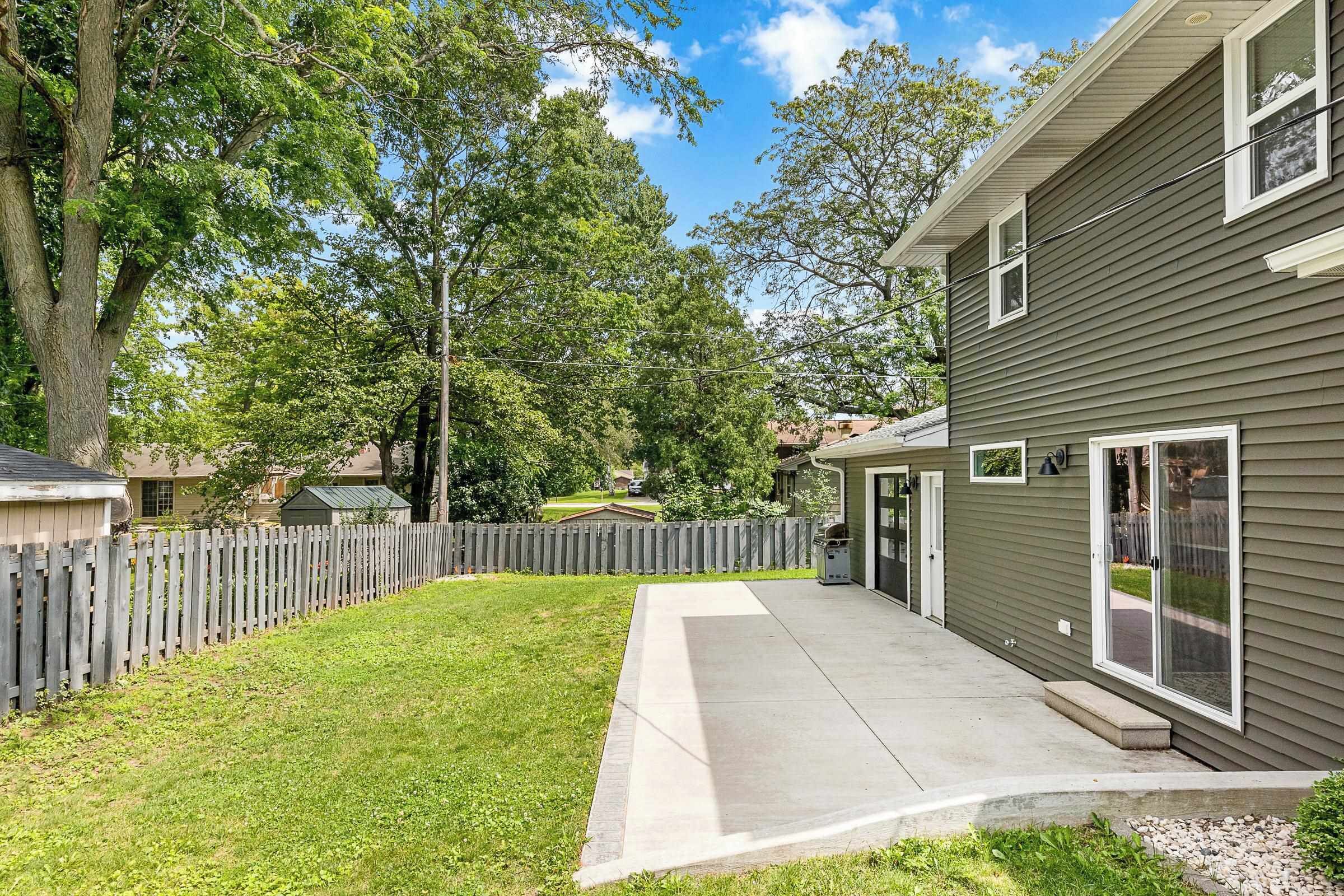 A residential property with a paved driveway, a wooden fence, and a grassy yard.