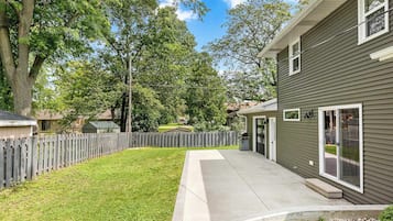 A residential property with a paved driveway, a wooden fence, and a grassy yard.