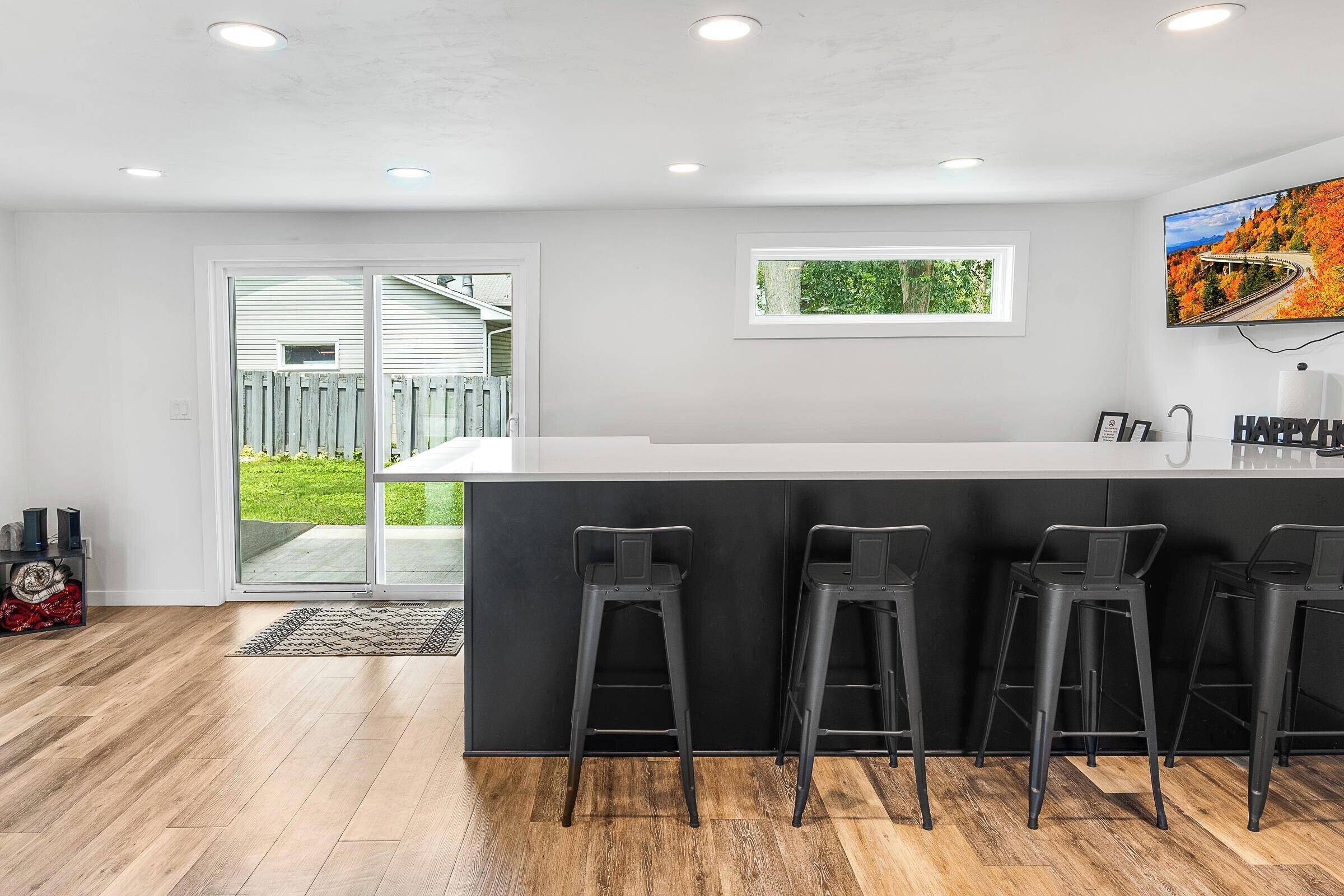 Una cocina moderna con una isla central, taburetes de bar, luces empotradas en el techo y vistas al exterior.