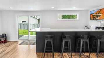 Una cocina moderna con una isla central, taburetes de bar, luces empotradas en el techo y vistas al exterior.