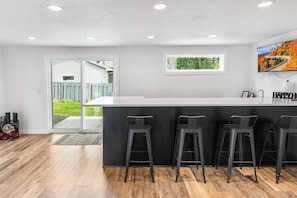 Una cucina moderna con isola centrale, sgabelli da bar, luci a incasso e vista sull'esterno.