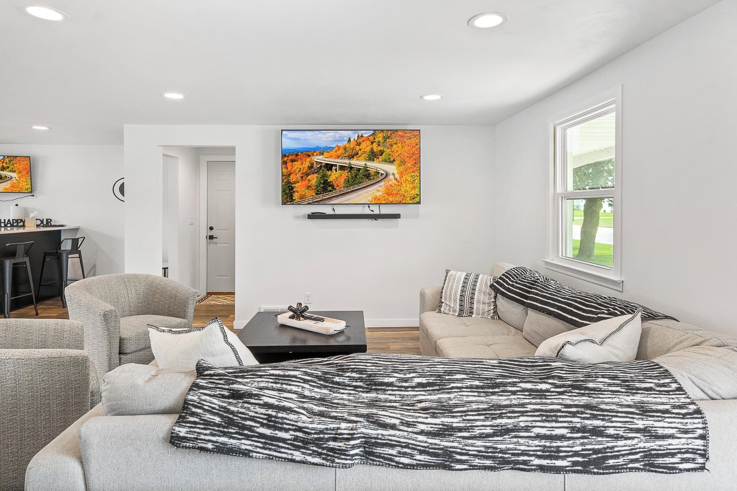 Una sala de estar moderna con sofá, sillones, una mesa de centro y un televisor montado en la pared.