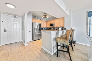 A modern kitchen with stainless steel appliances, a central island with bar stools, and wooden cabinetry. - Paradise at The Palms | Gulf Views, Resort Pool & Beach Gear (Destin)