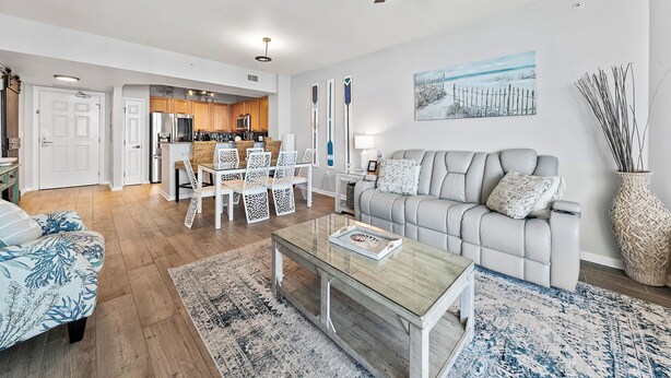 Een moderne woonkamer met een grijze bank, een salontafel en een eetgedeelte met rieten stoelen.