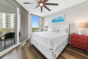 A bedroom with a bed, a nightstand, a red dresser, a ceiling fan, and a balcony with a chair. - Paradise at The Palms | Gulf Views, Resort Pool & Beach Gear (Destin)