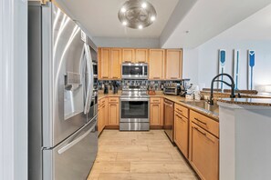 A modern kitchen with stainless steel appliances, wooden cabinets, and a granite countertop. - Paradise at The Palms | Gulf Views, Resort Pool & Beach Gear (Destin)