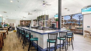 Een moderne bar met een centraal gelegen bar eiland, barkrukken en uitzicht op het strand door grote ramen.