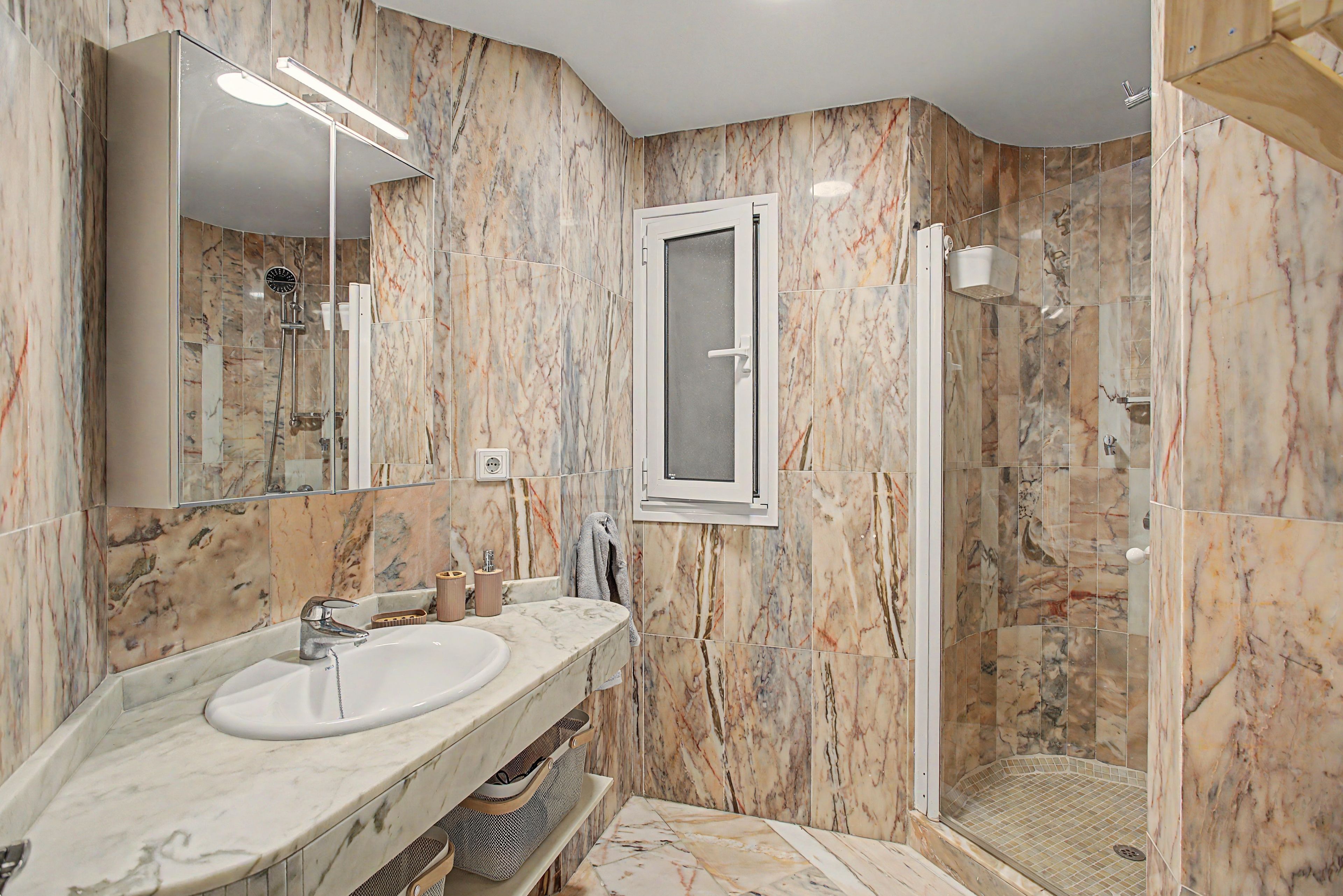 Un baño moderno con tocador de mármol, cabina de ducha de vidrio y un espejo grande.