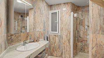 Un baño moderno con tocador de mármol, cabina de ducha de vidrio y un espejo grande.