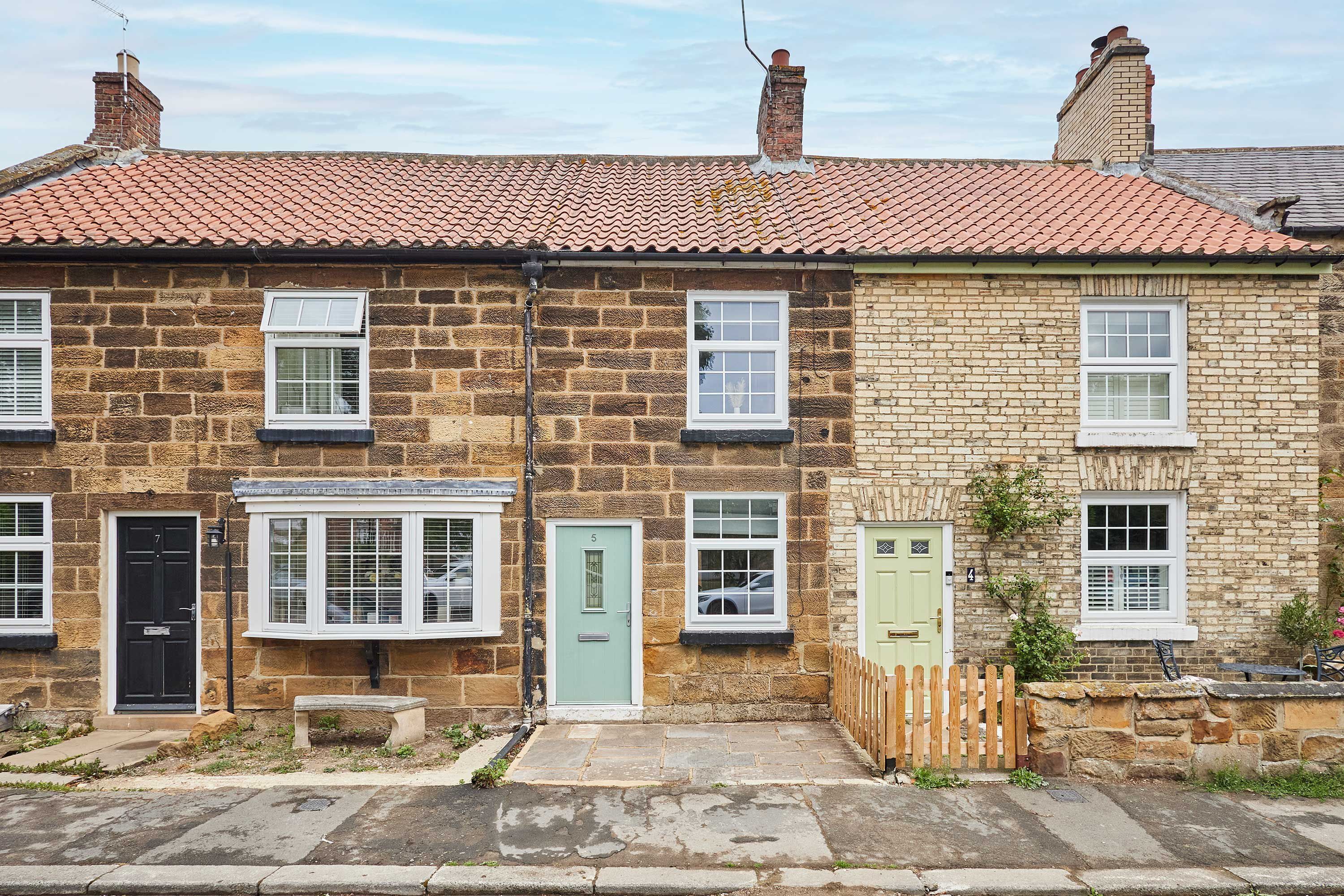 A row of terraced houses with brick walls, white-framed windows, and a tiled roof.