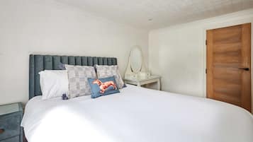 A neatly made bed with a white duvet, a dark green upholstered headboard, and decorative pillows.