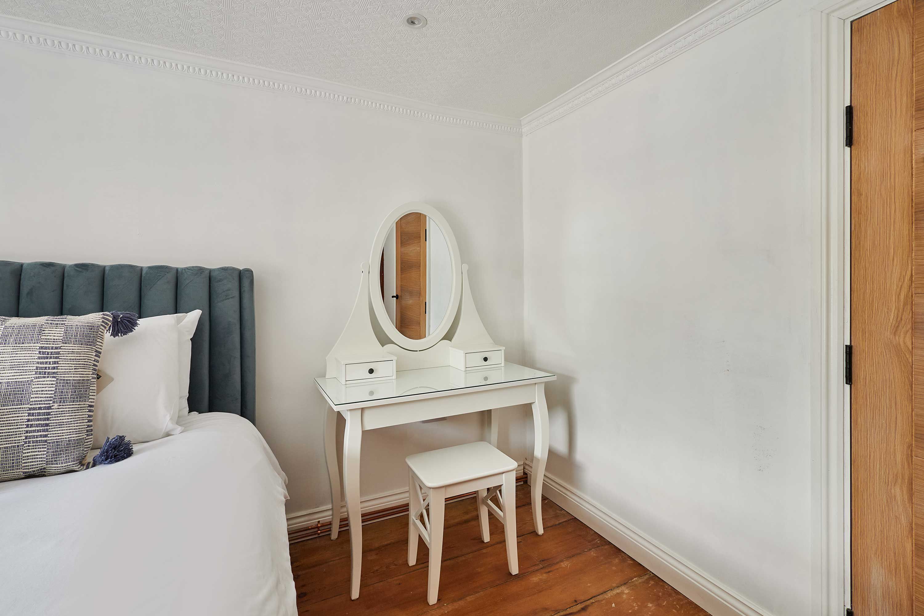A bedroom with a bed, a white dresser with a mirror, and a wooden door.