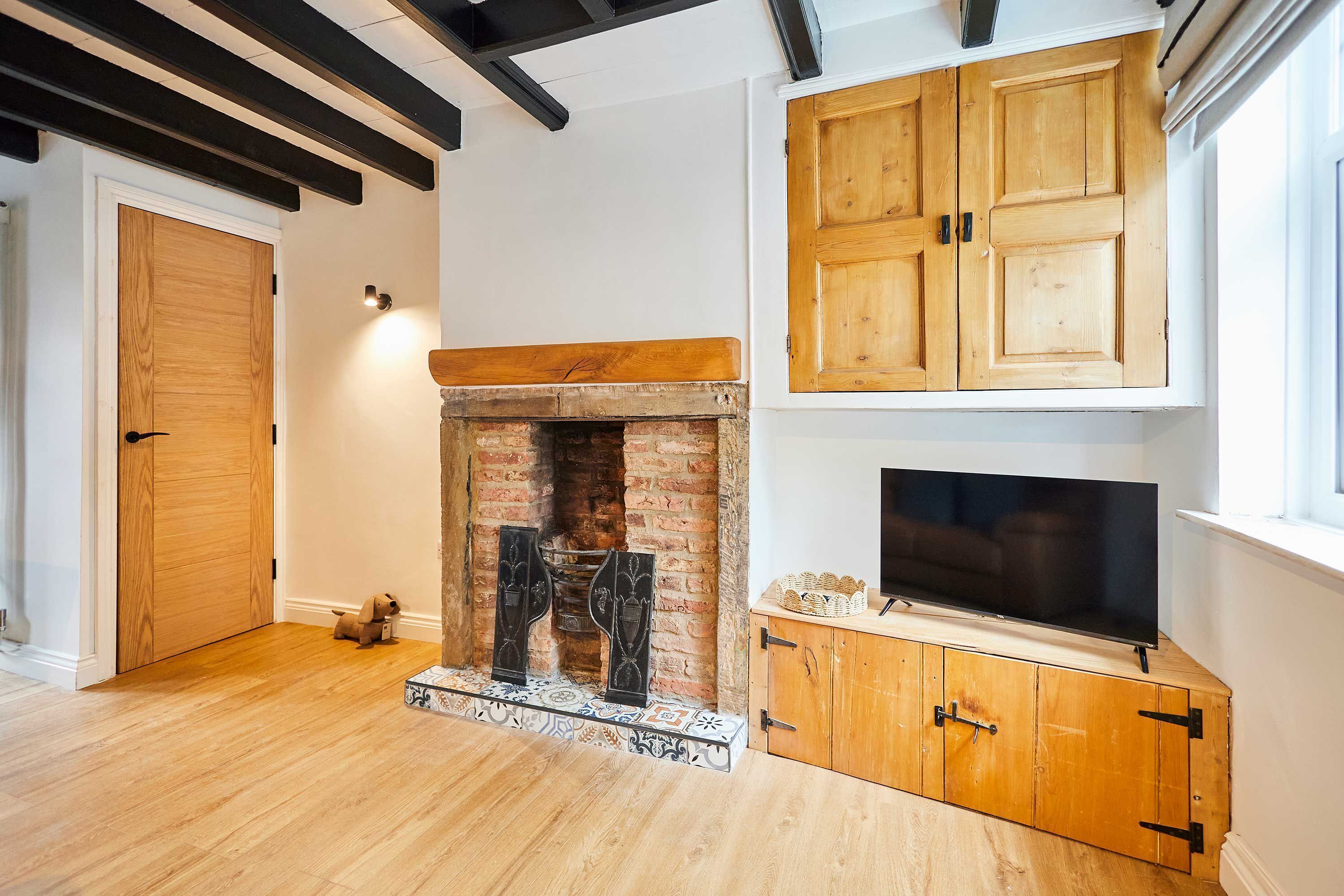 Een kamer met een open haard, houten kasten, een televisie en een deur.