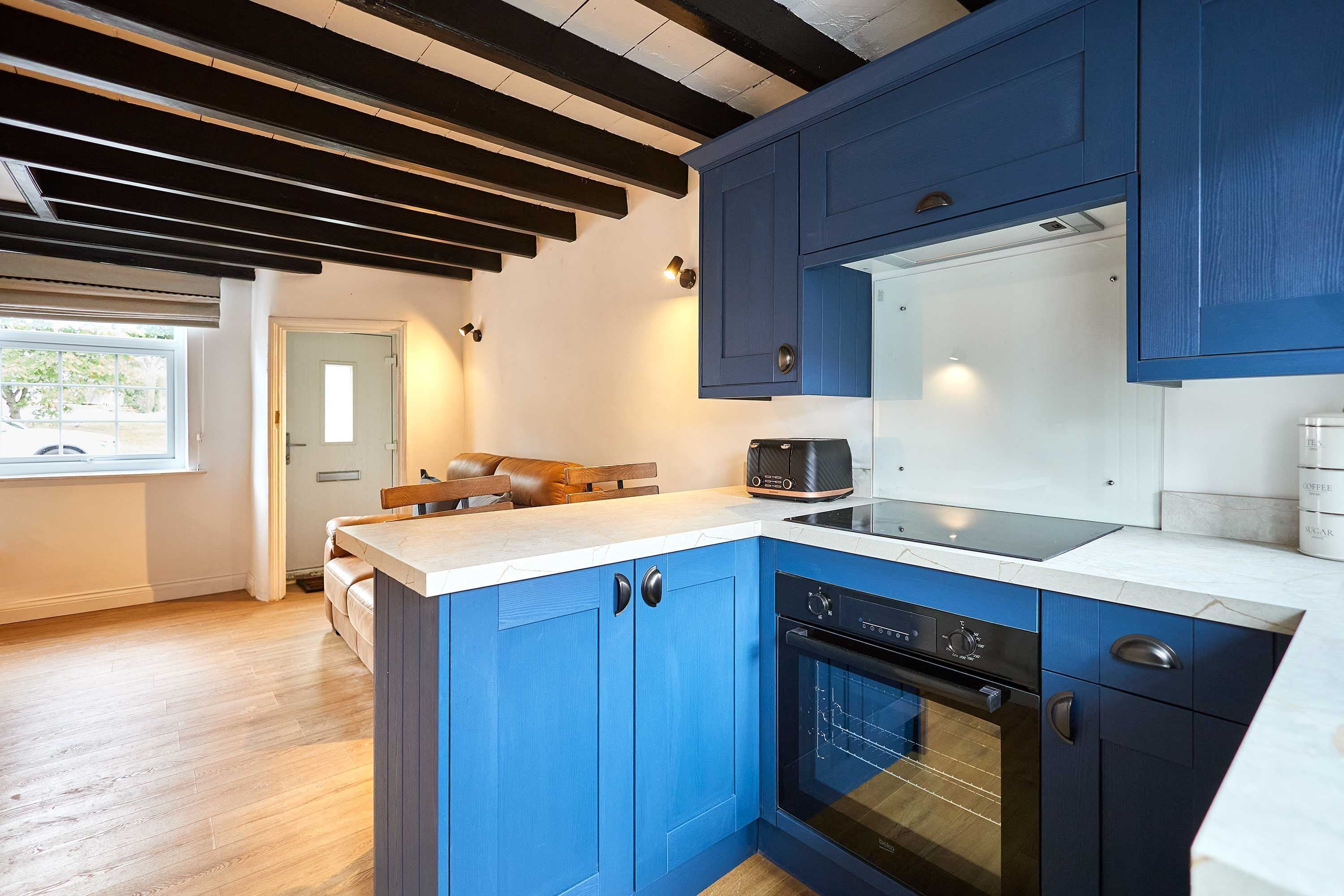 A modern kitchen with blue cabinets, a built-in oven, and a coffee maker.