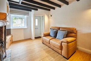 Uma sala de estar com sofá de couro, piso de madeira, lareira e janela com vista para o exterior.