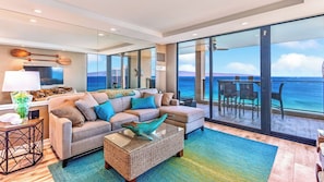 A modern living room with a large sofa, a coffee table, and a view of the ocean through large sliding doors. - Mahana | 4 Ocean View Villas, Sleeps 12 | Car Incl. w/ 6+ Nights | ML-4217 by KBM (Lahaina)