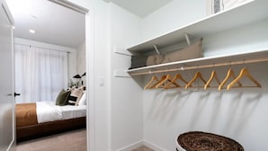 A bedroom with a bed, a closet with wooden hangers, and a wicker basket.