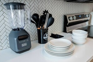 A kitchen with a blender, a utensil holder, and stacked plates.