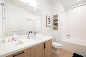 Un baño moderno con un lavabo blanco, un espejo, un inodoro y una zona de ducha.