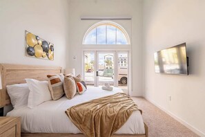 Un dormitorio con cama, almohadas, manta, televisor y ventana con vistas al exterior.