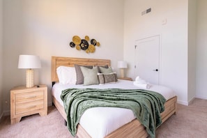 Quarto bem arrumado com uma cama, duas mesas de cabeceira, luminária na parede e uma porta.
