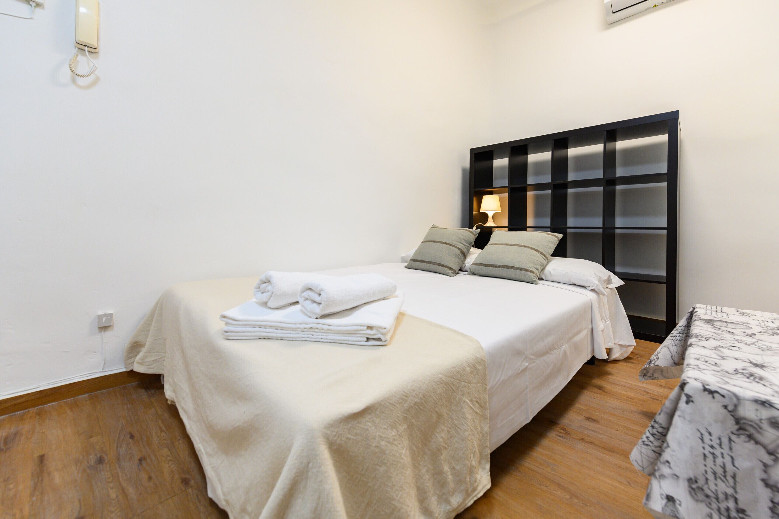Habitación de hotel con cama, mesita de noche, lámpara y aire acondicionado instalado en la pared.