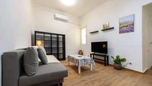 A modern living room with a grey sofa, a small table with a lamp, a TV on a stand, and a potted plant. - (MGU272D) 2-bedroom apartment in Chamberí (Madrid)