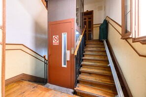 A staircase with wooden steps and a handrail, leading to a door with a fire safety sign. - (MGU272D) 2-bedroom apartment in Chamberí (Madrid)