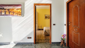 A hotel room with a bed, a chair, a small table with a plant, and a painting on the wall.