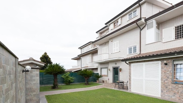 A two-story residential building with a well-maintained lawn, a patio area with outdoor furniture, and a garage with a large white door.