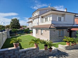 A two-story house with a stone facade, a tiled roof, and a well-maintained lawn with potted plants. - castelbarco house (Roma)