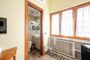 A bathroom with a toilet, sink, and shower area, a radiator, and a window with curtains. - castelbarco house (Roma)